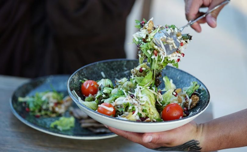 Colorful fresh garden salad with cherry tomatoes being served outdoors on a sunny day.