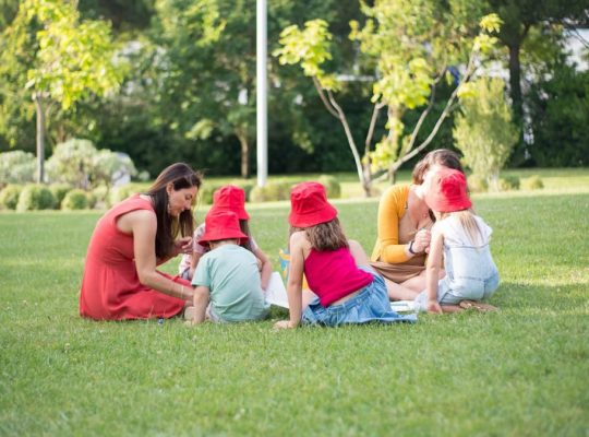 A family enjoys a summer picnic outdoors, bonding and relaxing in a sunny park setting.